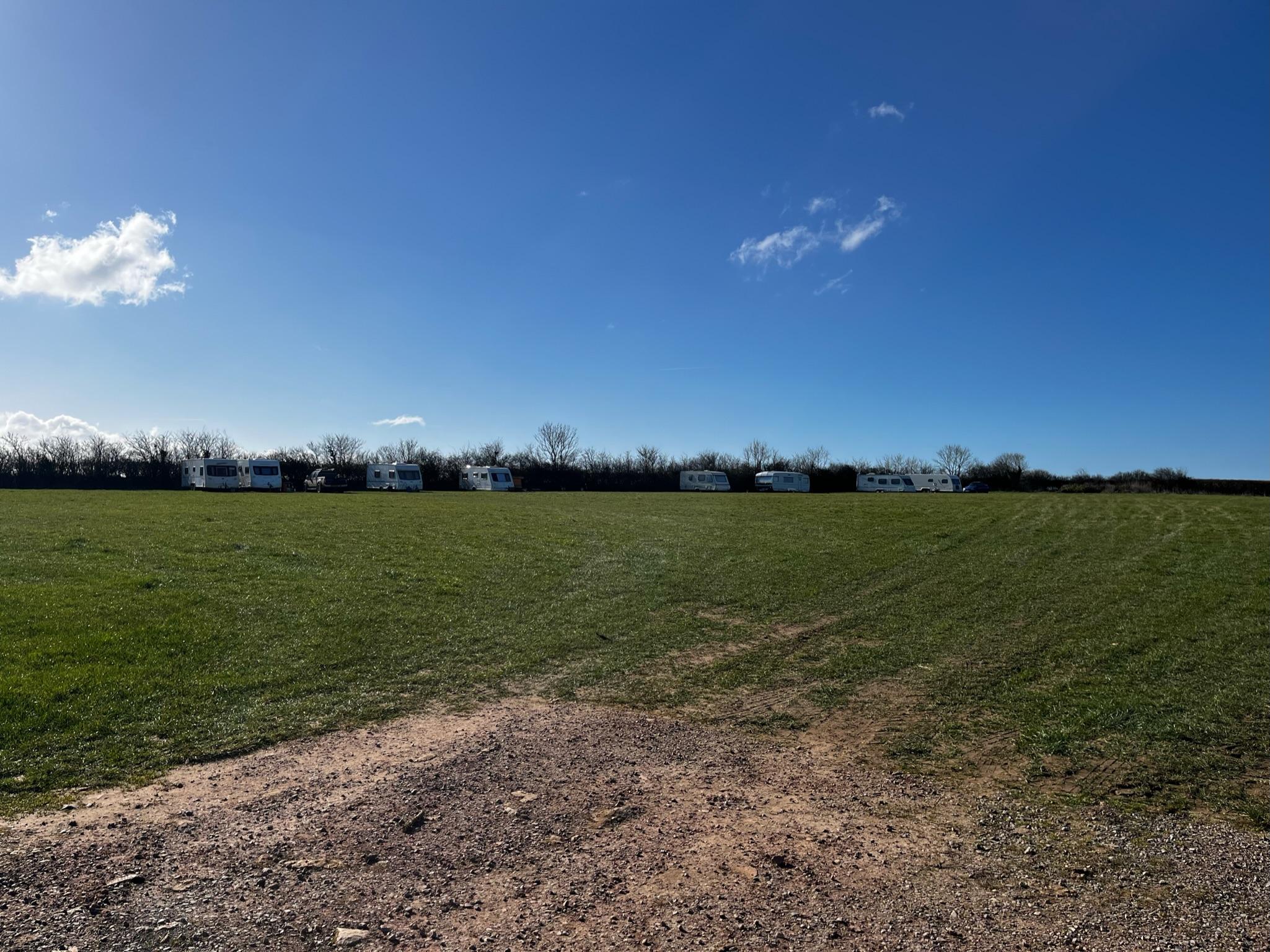 Wide shot of a camping field with 8 caravans parked along a hedge